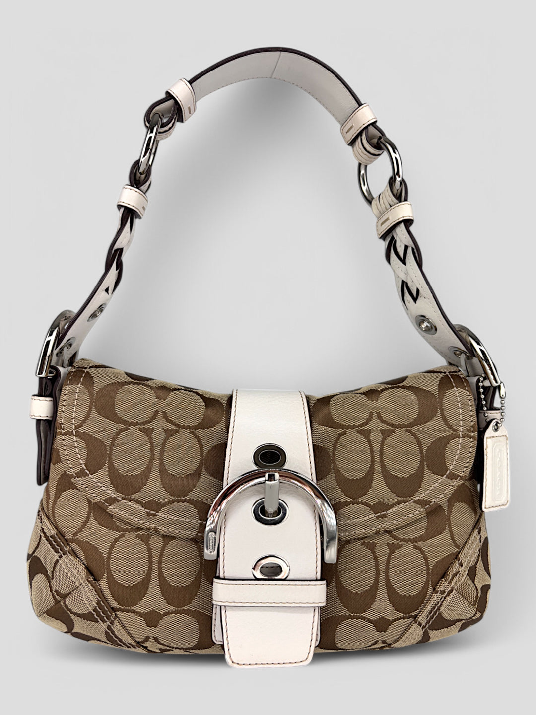 Coach Signature Strapbag mit beigem und braunem Logo-Muster, cremeweißen Lederdetails, silberfarbener Schnalle und geflochtenem Schulterriemen. Kompakt und stilvoll.