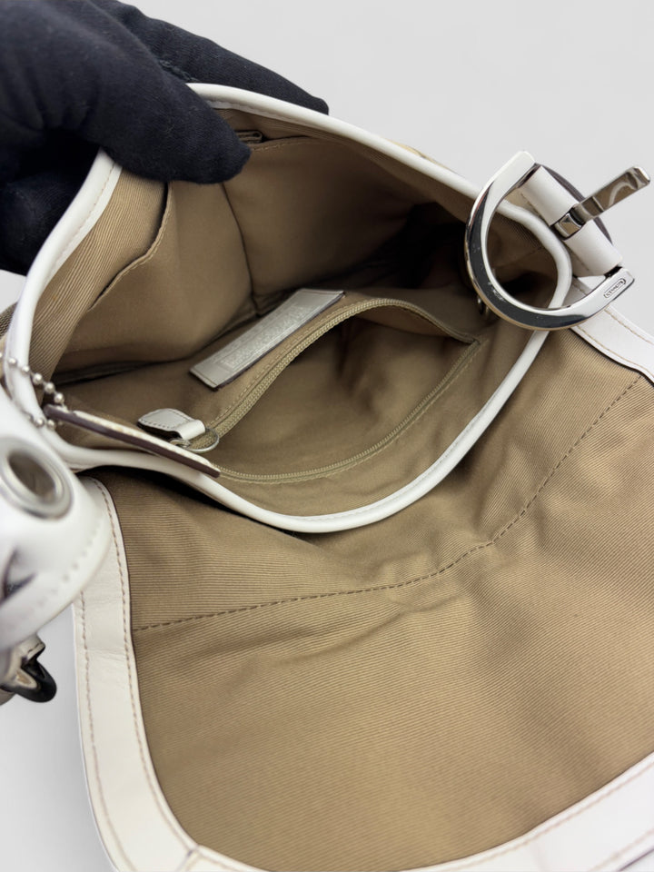 Coach Signature Strapbag mit beigem und braunem Logo-Muster, cremeweißen Lederdetails, silberfarbener Schnalle und geflochtenem Schulterriemen. Kompakt und stilvoll