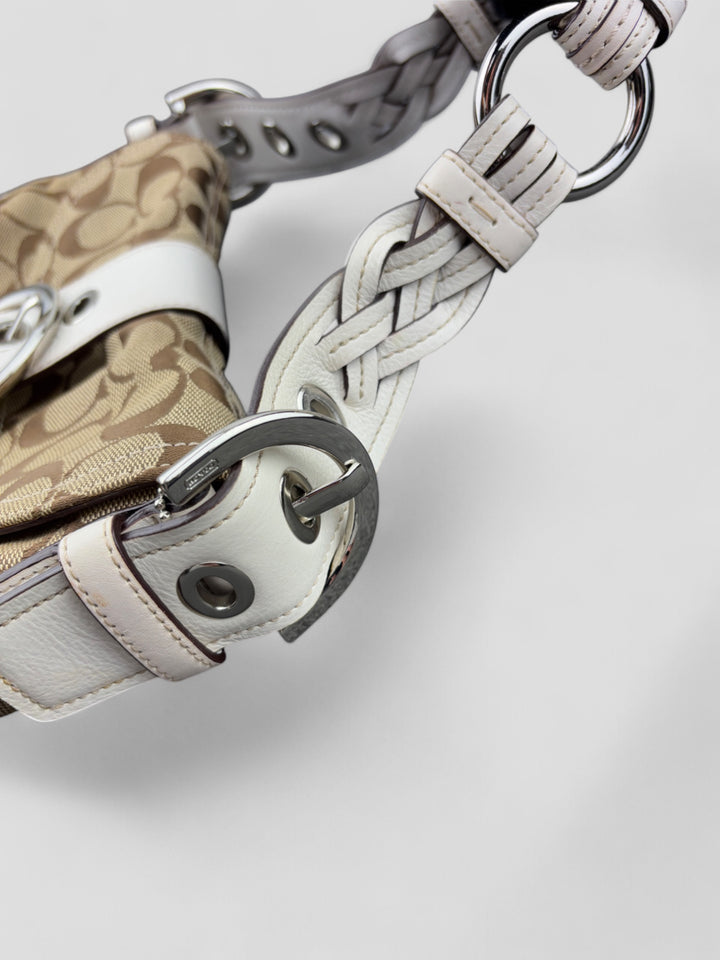 Coach Signature Strapbag mit beigem und braunem Logo-Muster, cremeweißen Lederdetails, silberfarbener Schnalle und geflochtenem Schulterriemen. Kompakt und stilvoll