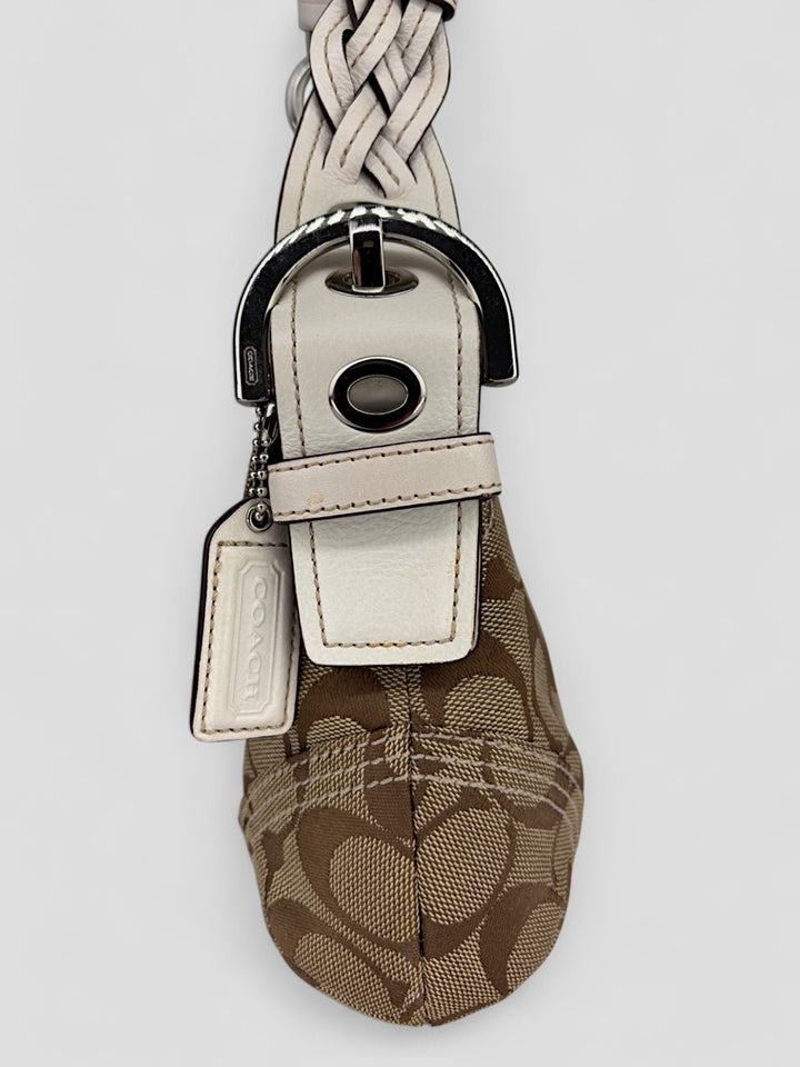 Coach Signature Strapbag mit beigem und braunem Logo-Muster, cremeweißen Lederdetails, silberfarbener Schnalle und geflochtenem Schulterriemen. Kompakt und stilvoll