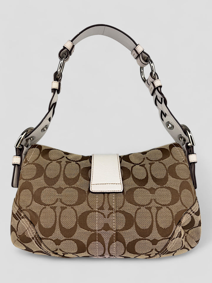 Coach Signature Strapbag mit beigem und braunem Logo-Muster, cremeweißen Lederdetails, silberfarbener Schnalle und geflochtenem Schulterriemen. Kompakt und stilvoll