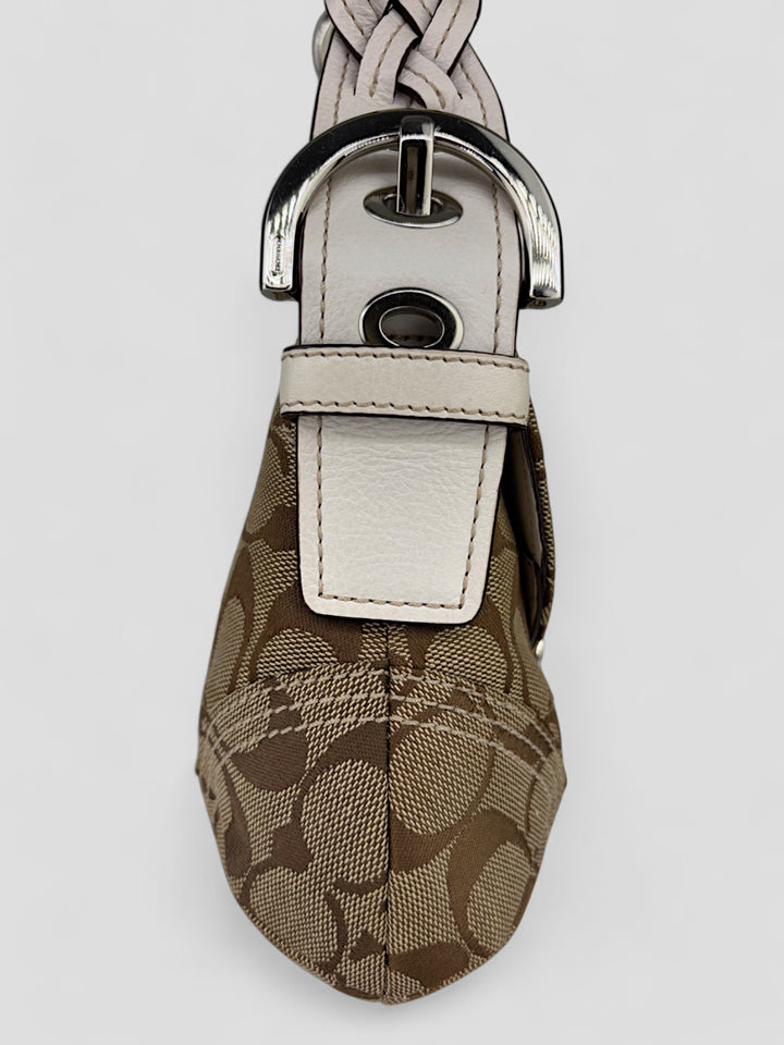 Coach Signature Strapbag mit beigem und braunem Logo-Muster, cremeweißen Lederdetails, silberfarbener Schnalle und geflochtenem Schulterriemen. Kompakt und stilvoll