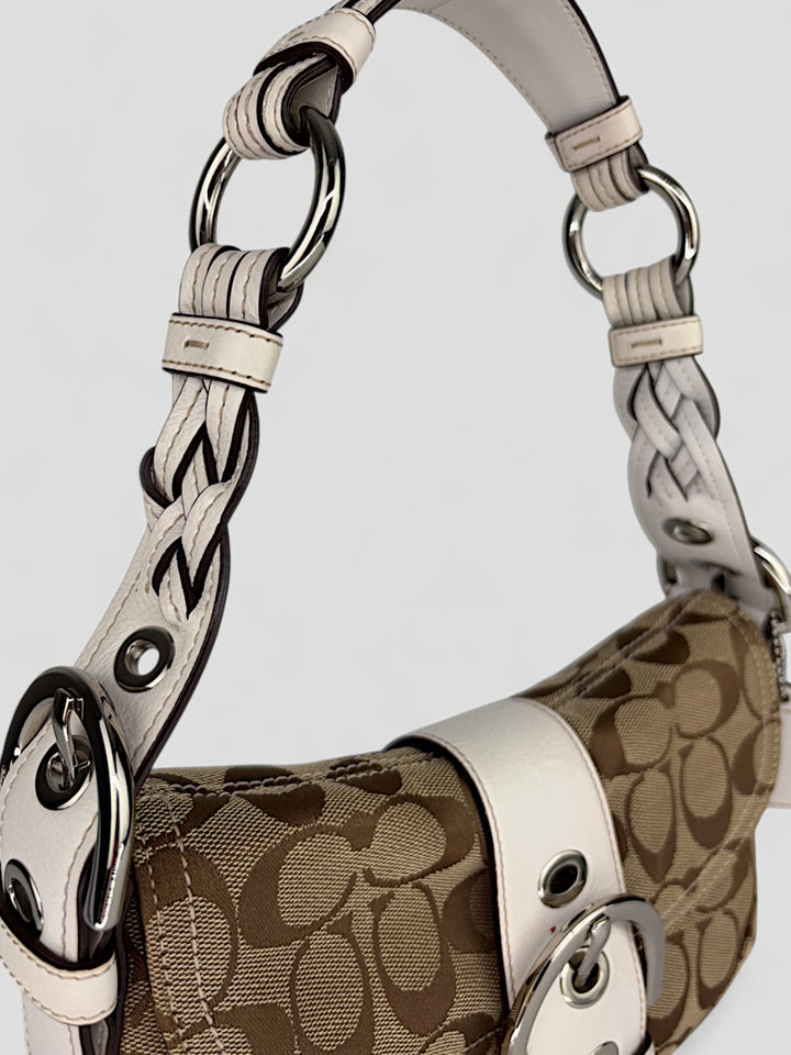 Coach Signature Strapbag mit beigem und braunem Logo-Muster, cremeweißen Lederdetails, silberfarbener Schnalle und geflochtenem Schulterriemen. Kompakt und stilvoll