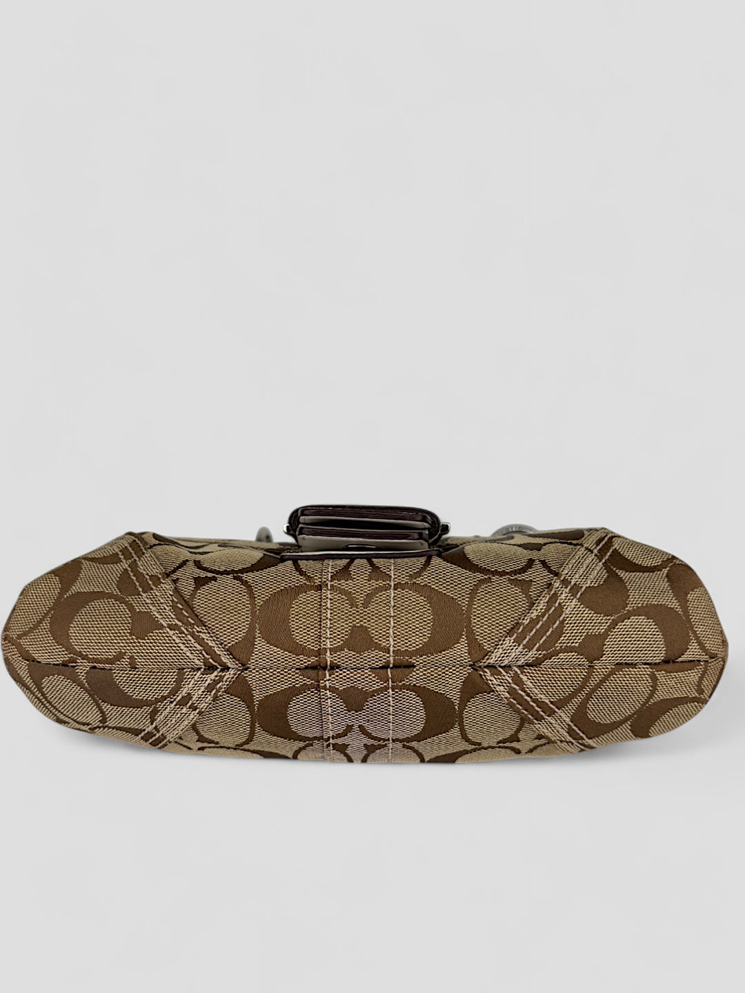 Coach Signature Strapbag mit beigem und braunem Logo-Muster, cremeweißen Lederdetails, silberfarbener Schnalle und geflochtenem Schulterriemen. Kompakt und stilvoll