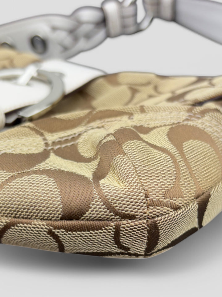 Coach Signature Strapbag mit beigem und braunem Logo-Muster, cremeweißen Lederdetails, silberfarbener Schnalle und geflochtenem Schulterriemen. Kompakt und stilvoll