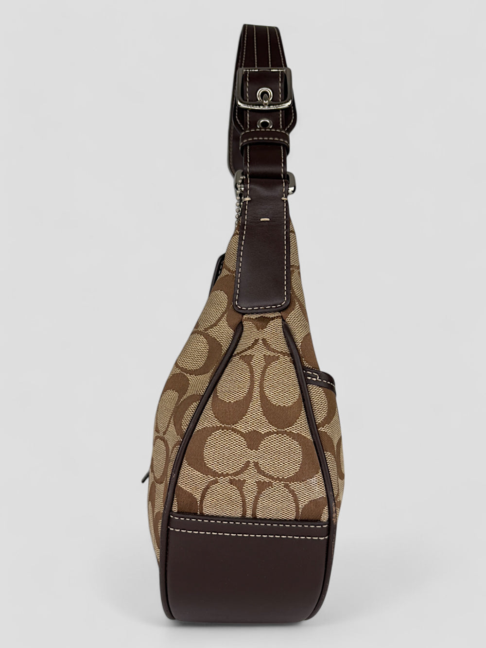 Coach Signature Strapbag mit beigem und braunem Logo-Muster, dunkelbraunen Lederdetails und einer Schnalle auf der Vorderseite. Verstellbare Schulterriemen für maximalen Komfort