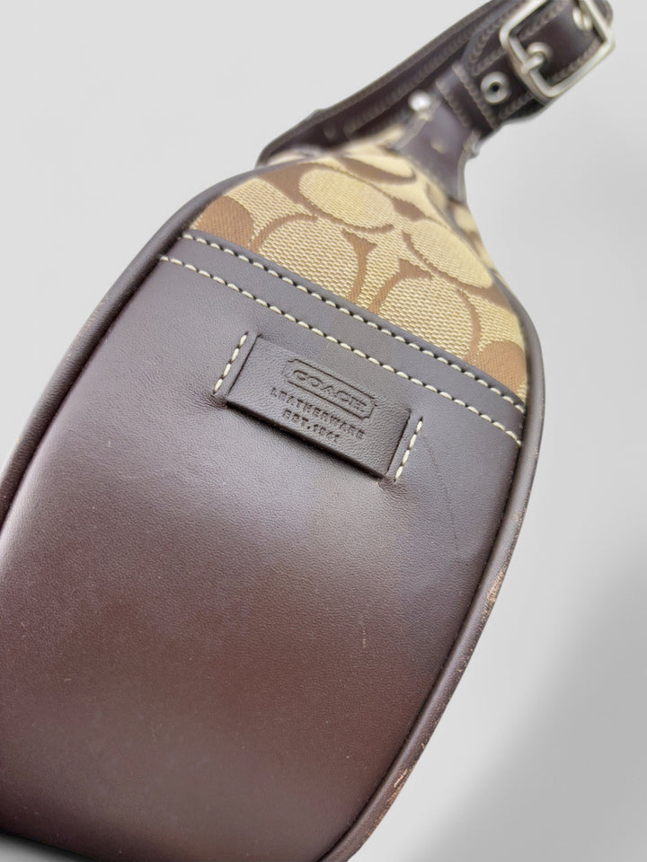 Coach Signature Strapbag mit beigem und braunem Logo-Muster, dunkelbraunen Lederdetails und einer Schnalle auf der Vorderseite. Verstellbare Schulterriemen für maximalen Komfort