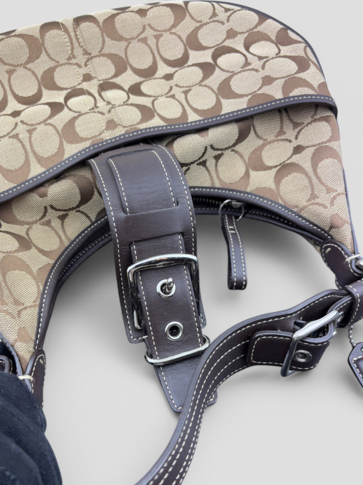 Coach Signature Strapbag mit beigem und braunem Logo-Muster, dunkelbraunen Lederdetails und einer Schnalle auf der Vorderseite. Verstellbare Schulterriemen für maximalen Komfort