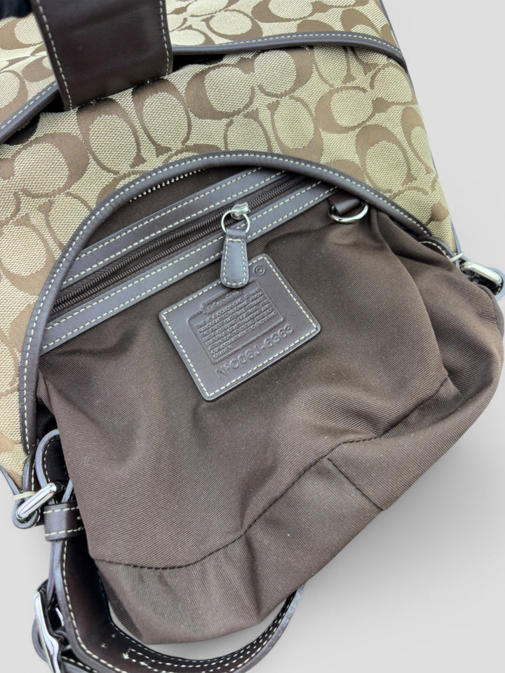 Coach Signature Strapbag mit beigem und braunem Logo-Muster, dunkelbraunen Lederdetails und einer Schnalle auf der Vorderseite. Verstellbare Schulterriemen für maximalen Komfort
