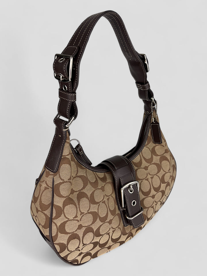 Coach Signature Strapbag mit beigem und braunem Logo-Muster, dunkelbraunen Lederdetails und einer Schnalle auf der Vorderseite. Verstellbare Schulterriemen für maximalen Komfort