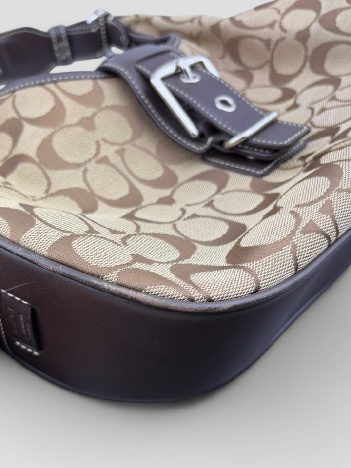 Coach Signature Strapbag mit beigem und braunem Logo-Muster, dunkelbraunen Lederdetails und einer Schnalle auf der Vorderseite. Verstellbare Schulterriemen für maximalen Komfort