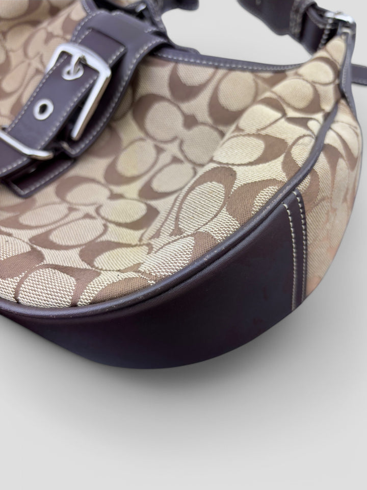 Coach Signature Strapbag mit beigem und braunem Logo-Muster, dunkelbraunen Lederdetails und einer Schnalle auf der Vorderseite. Verstellbare Schulterriemen für maximalen Komfort