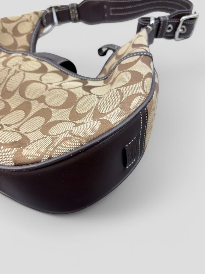 Coach Signature Strapbag mit beigem und braunem Logo-Muster, dunkelbraunen Lederdetails und einer Schnalle auf der Vorderseite. Verstellbare Schulterriemen für maximalen Komfort