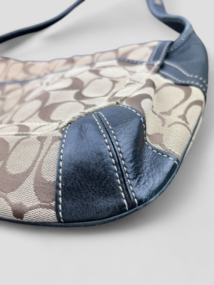 Coach Tasche mit beigem und braunem Logo-Muster, tiefschwarzen Lederdetails, goldfarbenen Beschlägen und einer markanten Schnalle. Stilvoll und luxuriös