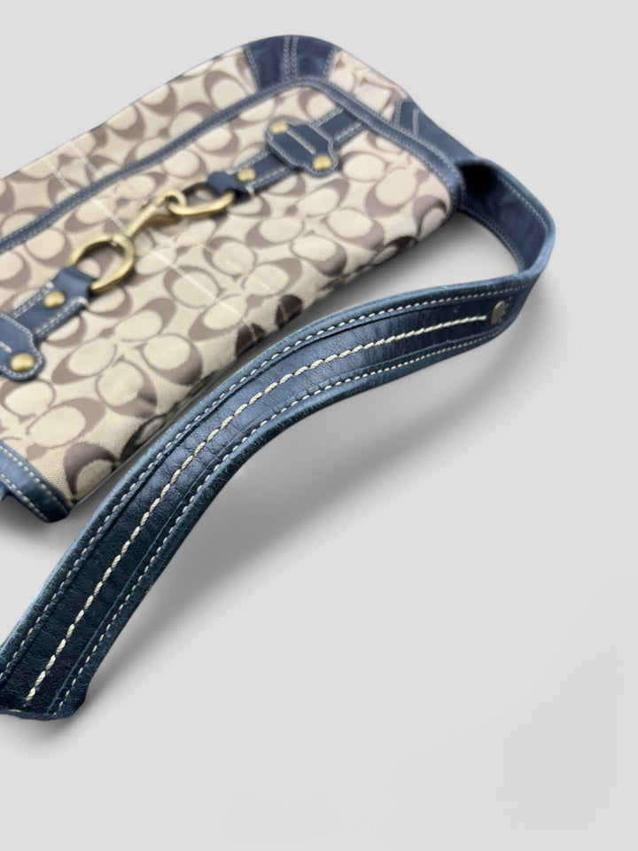 Coach Tasche mit beigem und braunem Logo-Muster, tiefschwarzen Lederdetails, goldfarbenen Beschlägen und einer markanten Schnalle. Stilvoll und luxuriös
