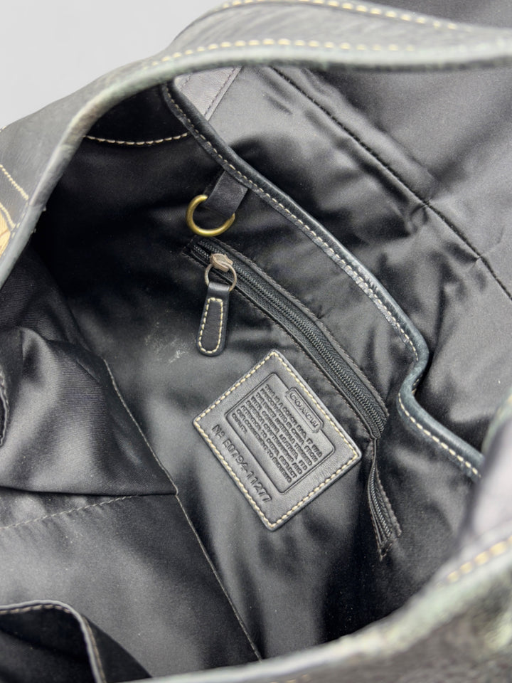 Coach Tasche mit beigem und braunem Logo-Muster, tiefschwarzen Lederdetails, goldfarbenen Beschlägen und einer markanten Schnalle. Stilvoll und luxuriös