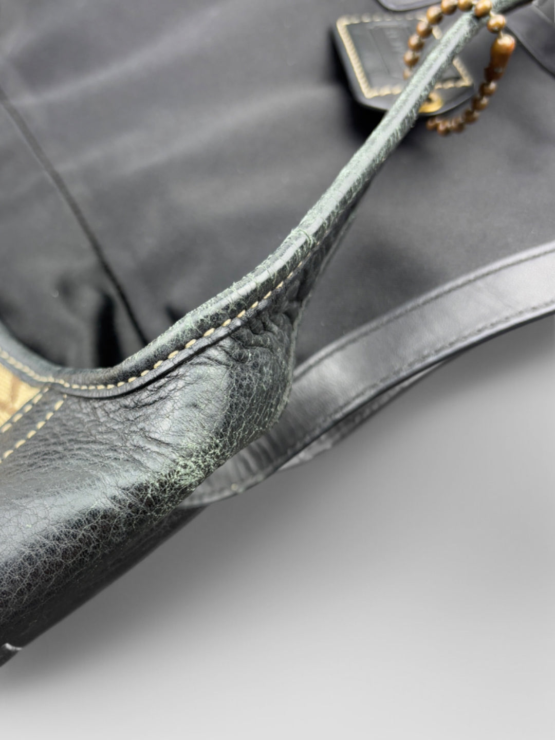 Coach Tasche mit beigem und braunem Logo-Muster, tiefschwarzen Lederdetails, goldfarbenen Beschlägen und einer markanten Schnalle. Stilvoll und luxuriös