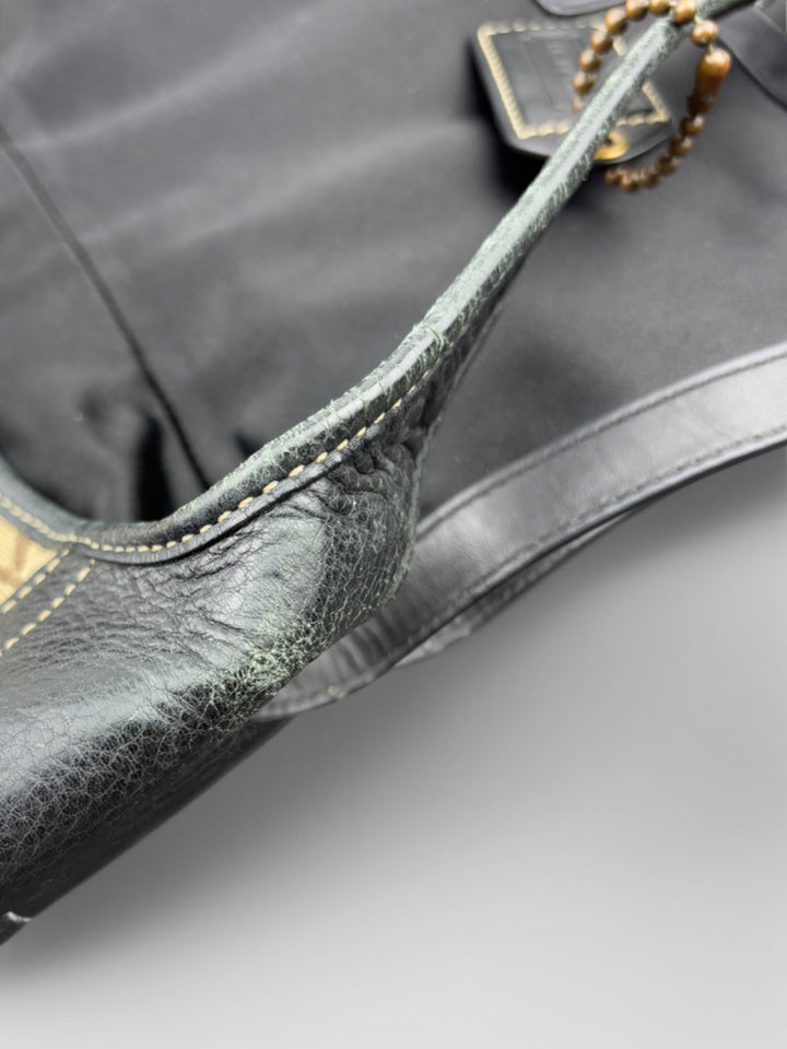 Coach Tasche mit beigem und braunem Logo-Muster, tiefschwarzen Lederdetails, goldfarbenen Beschlägen und einer markanten Schnalle. Stilvoll und luxuriös