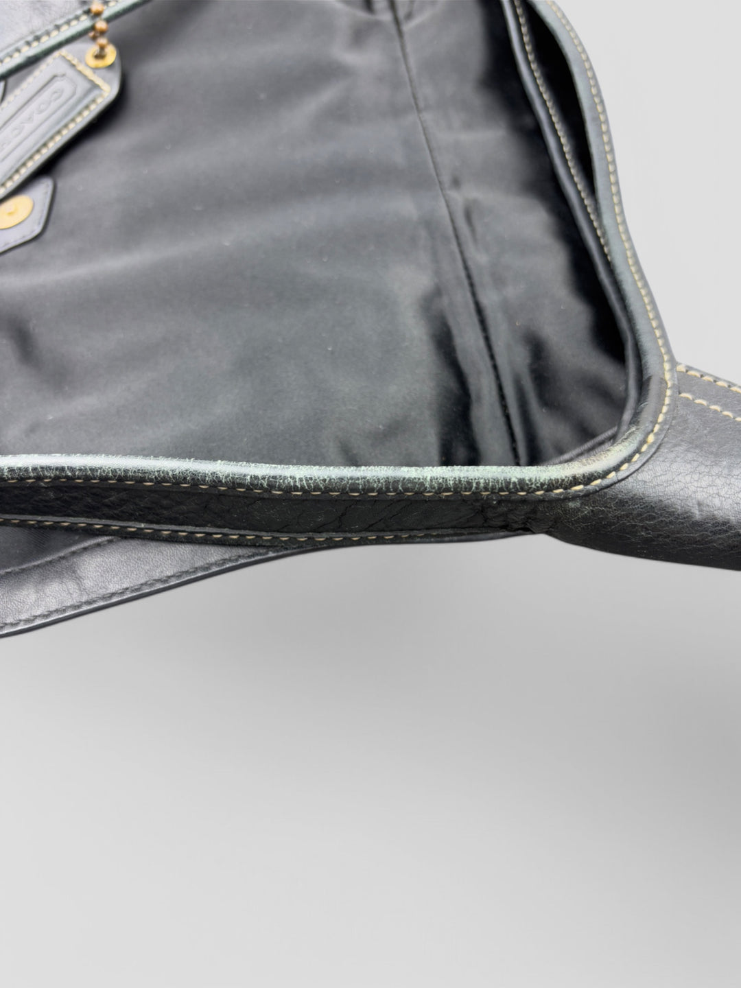 Coach Tasche mit beigem und braunem Logo-Muster, tiefschwarzen Lederdetails, goldfarbenen Beschlägen und einer markanten Schnalle. Stilvoll und luxuriös