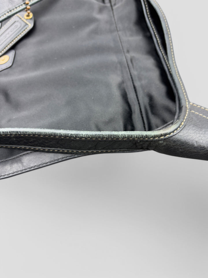 Coach Tasche mit beigem und braunem Logo-Muster, tiefschwarzen Lederdetails, goldfarbenen Beschlägen und einer markanten Schnalle. Stilvoll und luxuriös