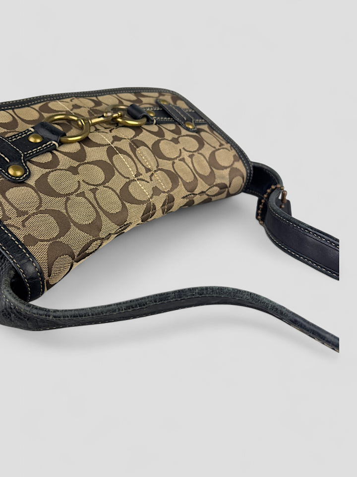 Coach Tasche mit beigem und braunem Logo-Muster, tiefschwarzen Lederdetails, goldfarbenen Beschlägen und einer markanten Schnalle. Stilvoll und luxuriös