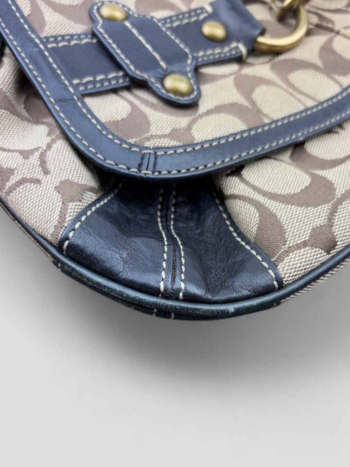 Coach Tasche mit beigem und braunem Logo-Muster, tiefschwarzen Lederdetails, goldfarbenen Beschlägen und einer markanten Schnalle. Stilvoll und luxuriös