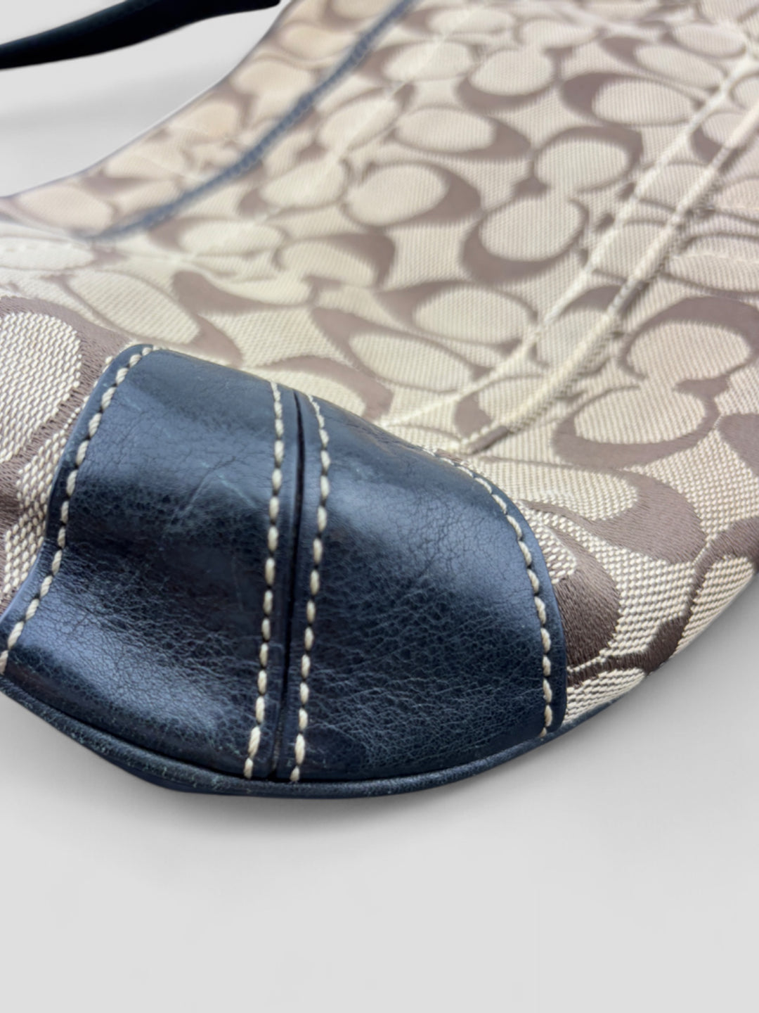 Coach Tasche mit beigem und braunem Logo-Muster, tiefschwarzen Lederdetails, goldfarbenen Beschlägen und einer markanten Schnalle. Stilvoll und luxuriös