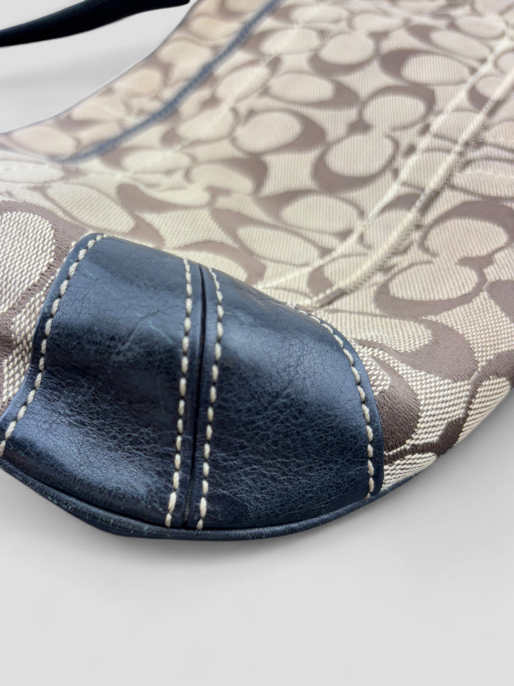 Coach Tasche mit beigem und braunem Logo-Muster, tiefschwarzen Lederdetails, goldfarbenen Beschlägen und einer markanten Schnalle. Stilvoll und luxuriös