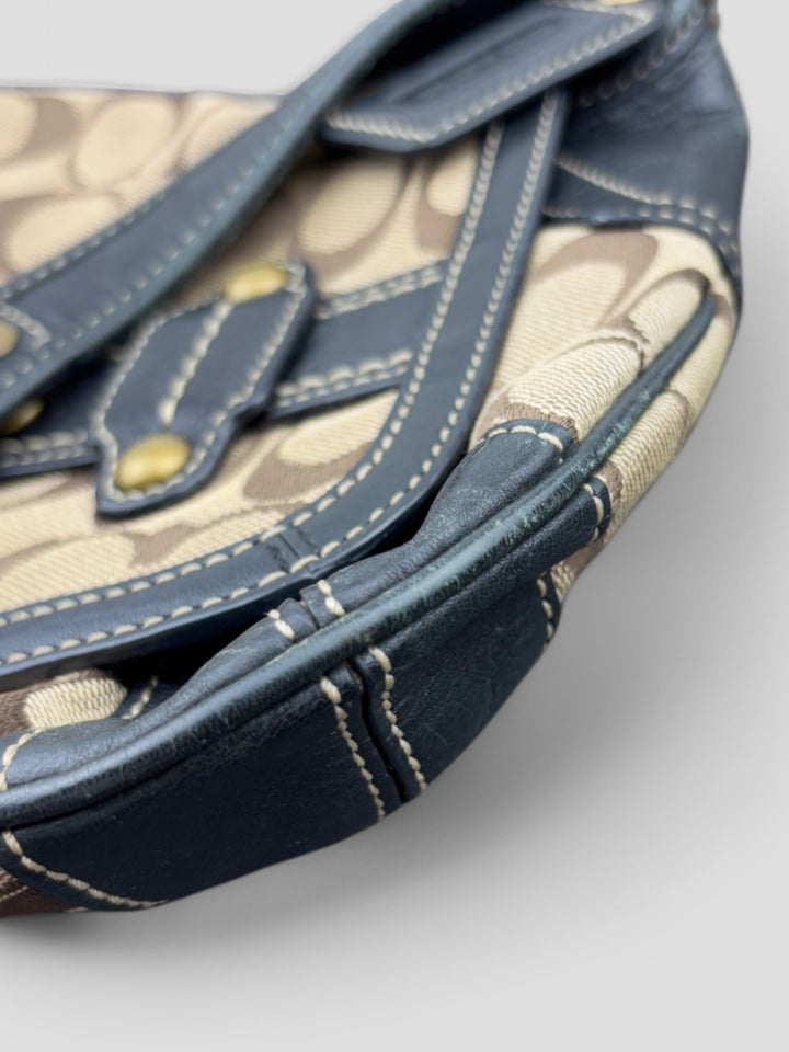 Coach Tasche mit beigem und braunem Logo-Muster, tiefschwarzen Lederdetails, goldfarbenen Beschlägen und einer markanten Schnalle. Stilvoll und luxuriös