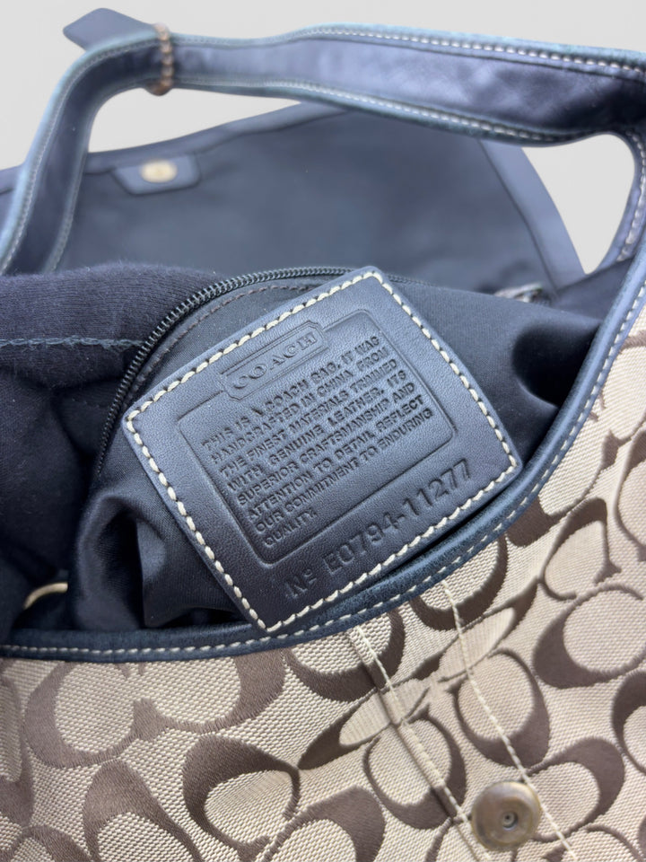 Coach Tasche mit beigem und braunem Logo-Muster, tiefschwarzen Lederdetails, goldfarbenen Beschlägen und einer markanten Schnalle. Stilvoll und luxuriös