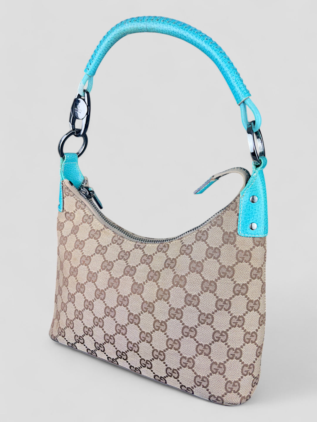 Gucci Hobo Tasche aus beigem Canvas mit GG-Muster, akzentuiert durch türkisfarbene Lederdetails und silberfarbene Metall-Elemente. Stilvoll und modern