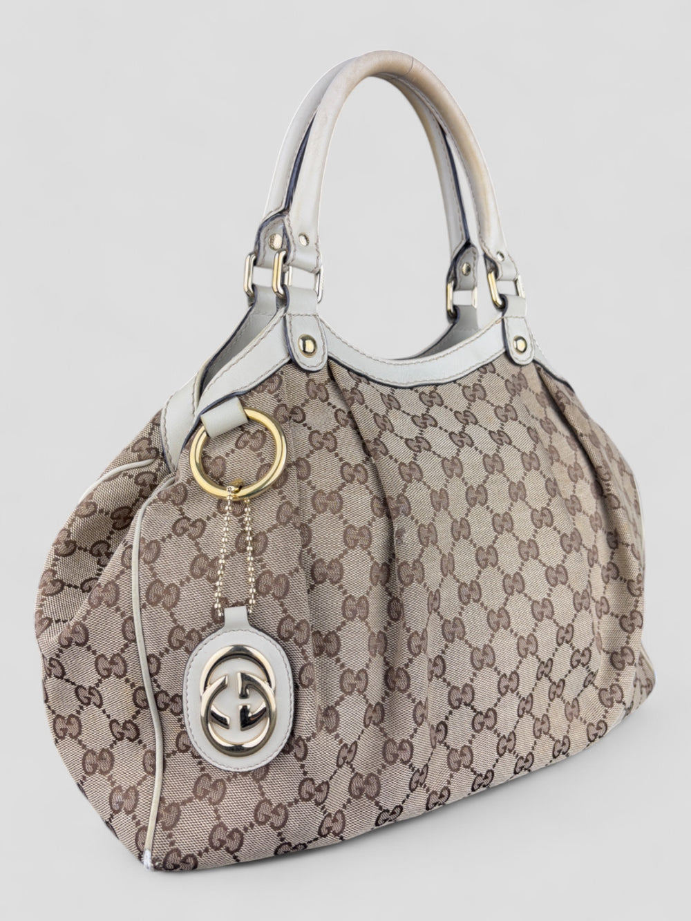 Gucci Sukey Tasche aus cremefarbenem GG-Canvas, ergänzt durch hochwertige Lederdetails und einen abnehmbaren Gucci-Anhänger