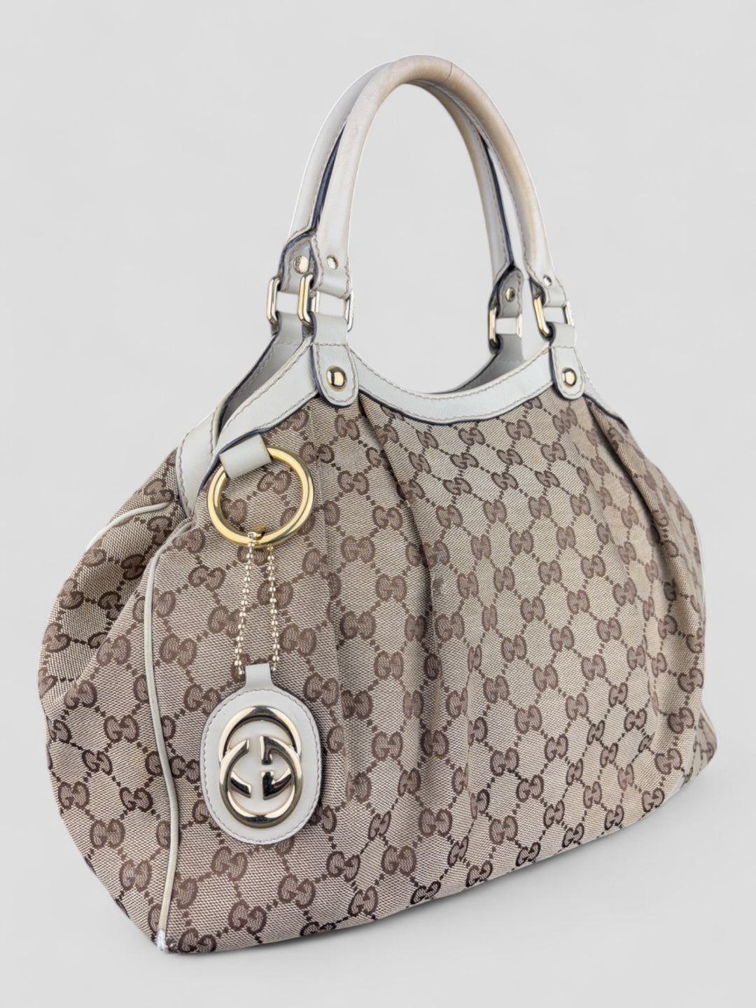 Gucci Sukey Tasche aus cremefarbenem GG-Canvas, ergänzt durch hochwertige Lederdetails und einen abnehmbaren Gucci-Anhänger
